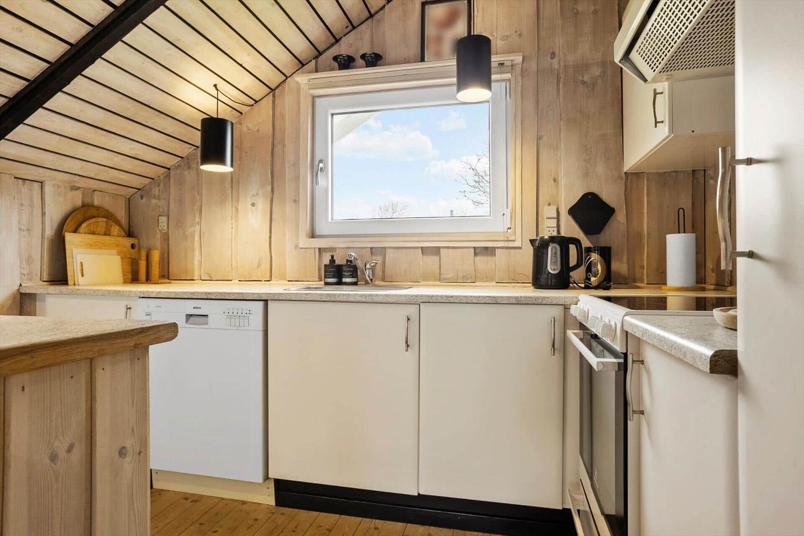 Küche mit Holzwand, Fenster, Spüle, Kühlschrank und Kochfeld.