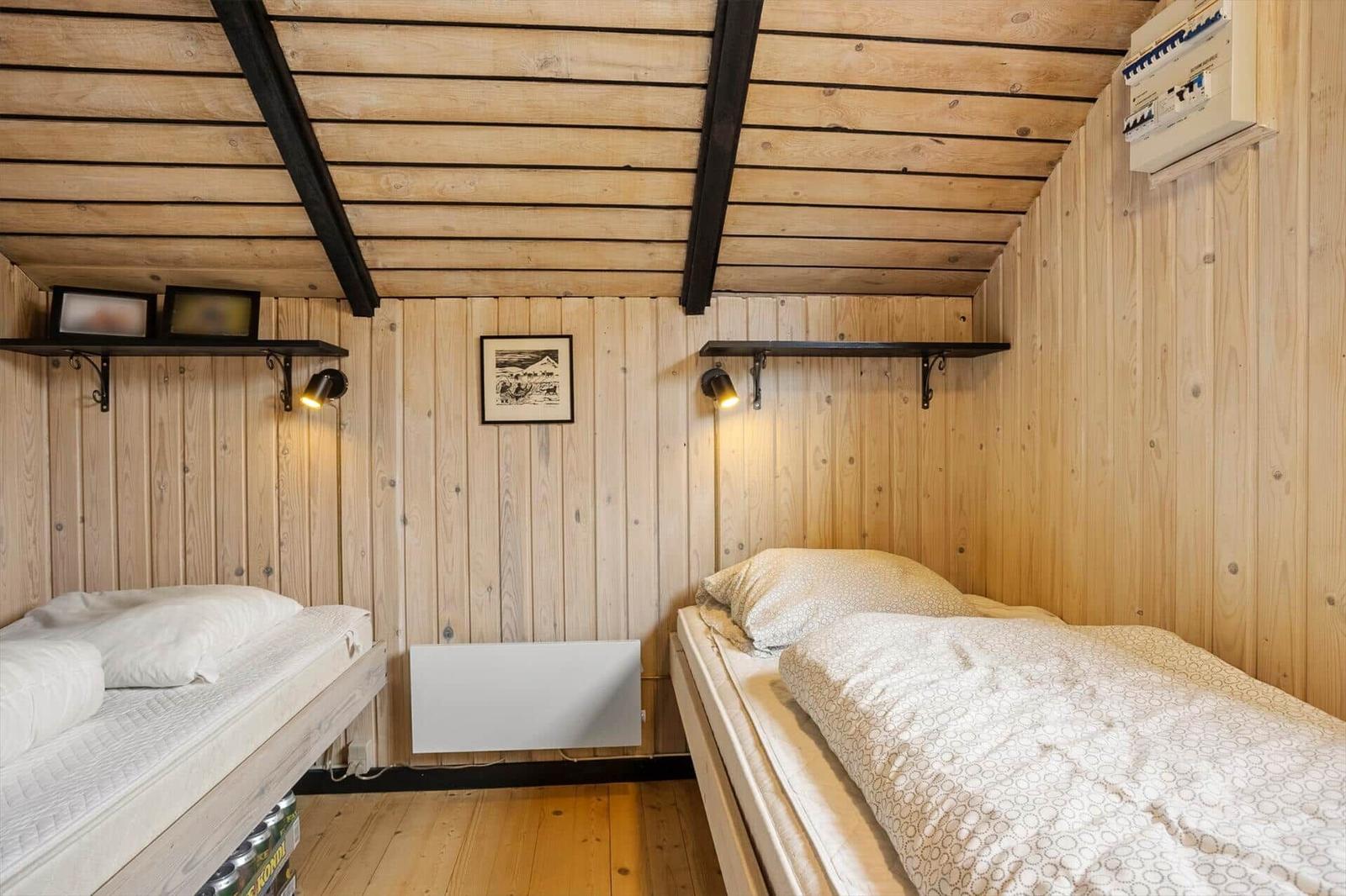 Zwei Betten in einem holzverkleideten Raum mit Deckenbalken und Wandregalen.