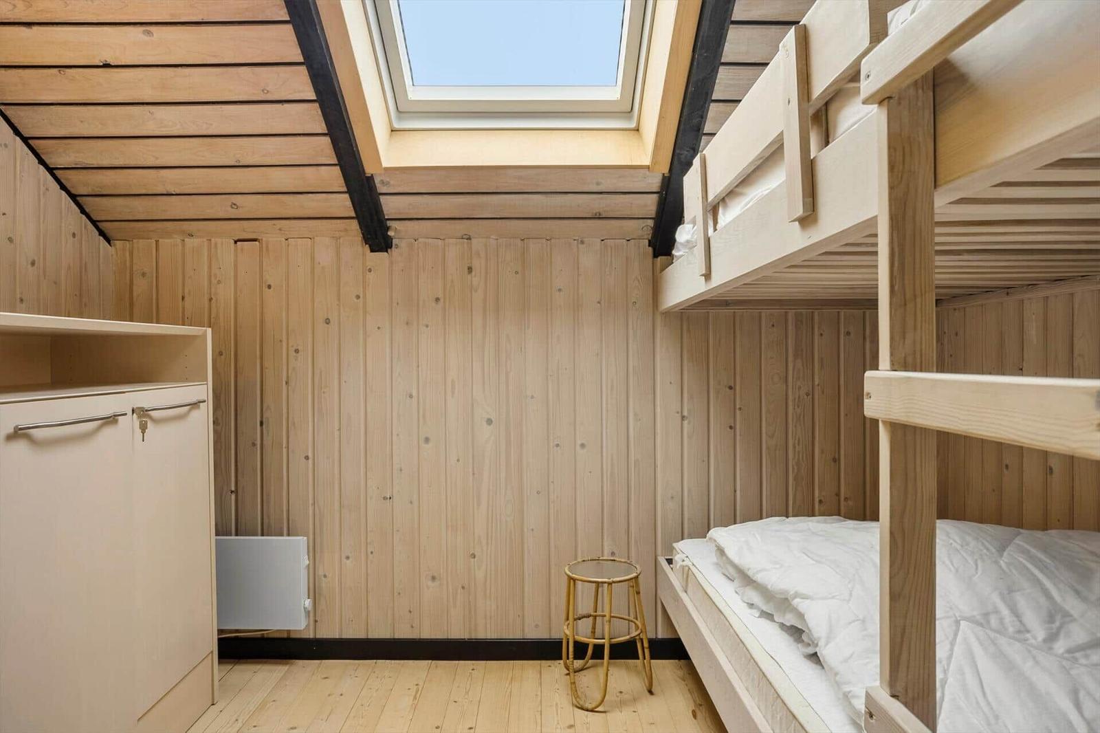 Zimmer mit Holzwand, Doppelstockbett und Dachfenster.