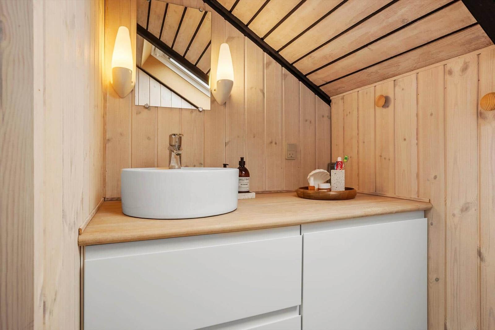 Badezimmer mit Waschbecken, Spiegel und Holzwand