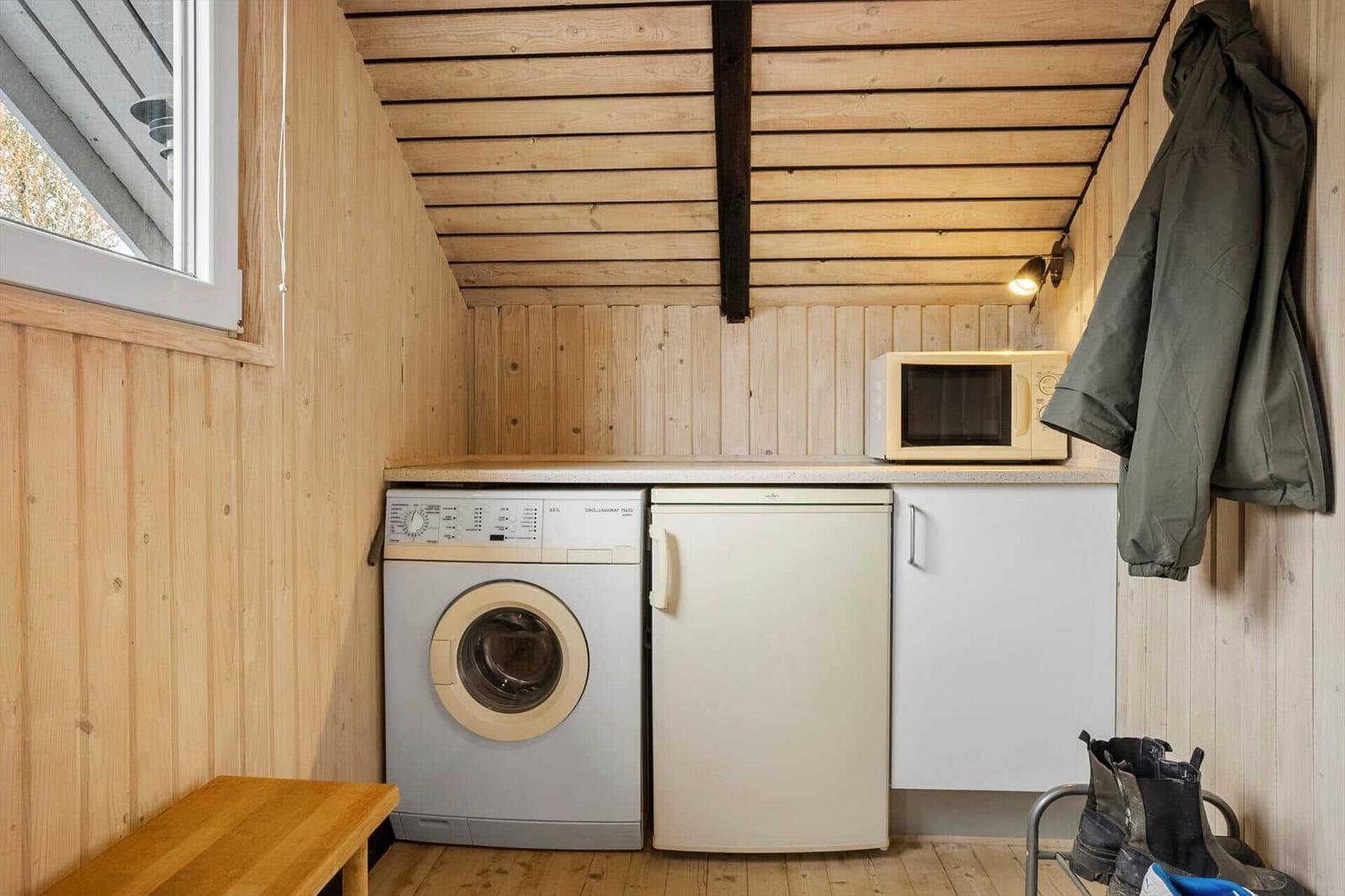 Kleine Küche mit Waschmaschine, Spülmaschine und Mikrowelle. Holzwände und -decke.