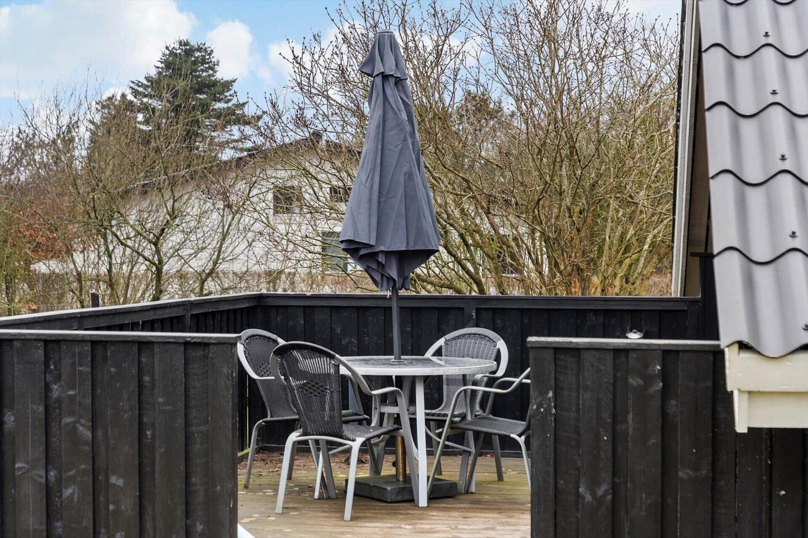 Terrasse mit Tisch, Stühlen und geschlossenem Sonnenschirm.