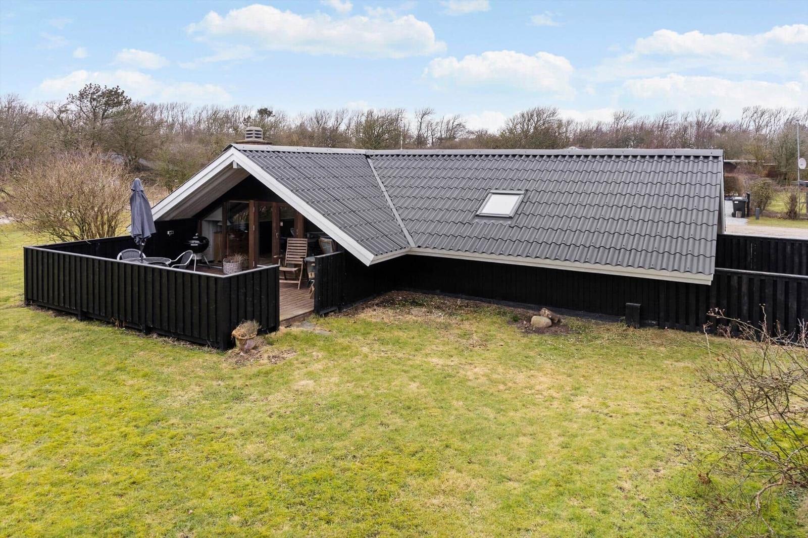Moderne Hütte mit Terrasse, Grill und Garten. Dach mit Dachfenster. Umgeben von Wald.