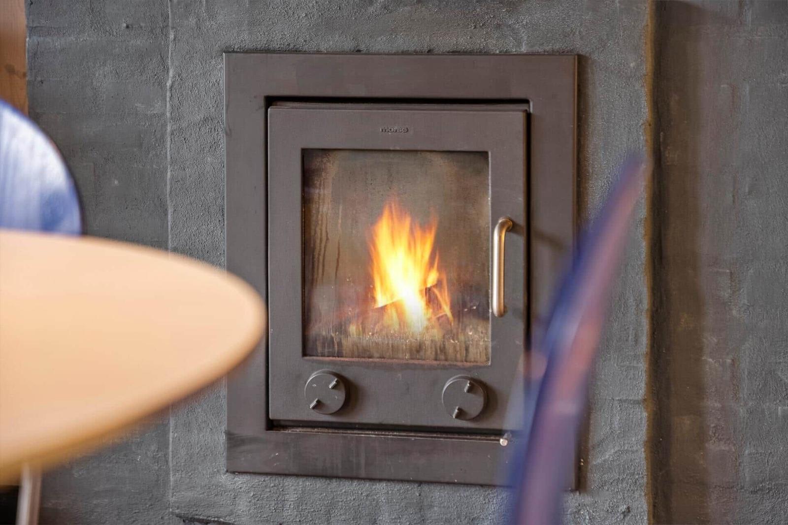 Ein Kamin mit brennendem Holz in einer Wand aus Beton.