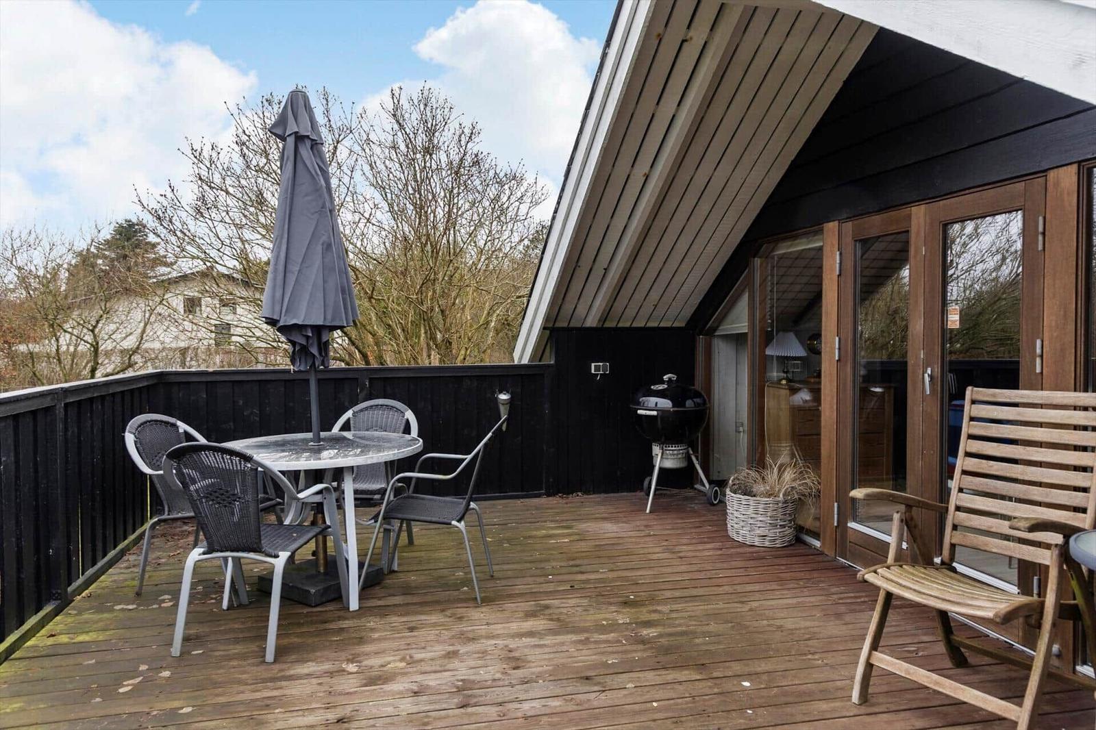 Terrasse mit Tisch, Stühlen, Sonnenschirm und Grill.