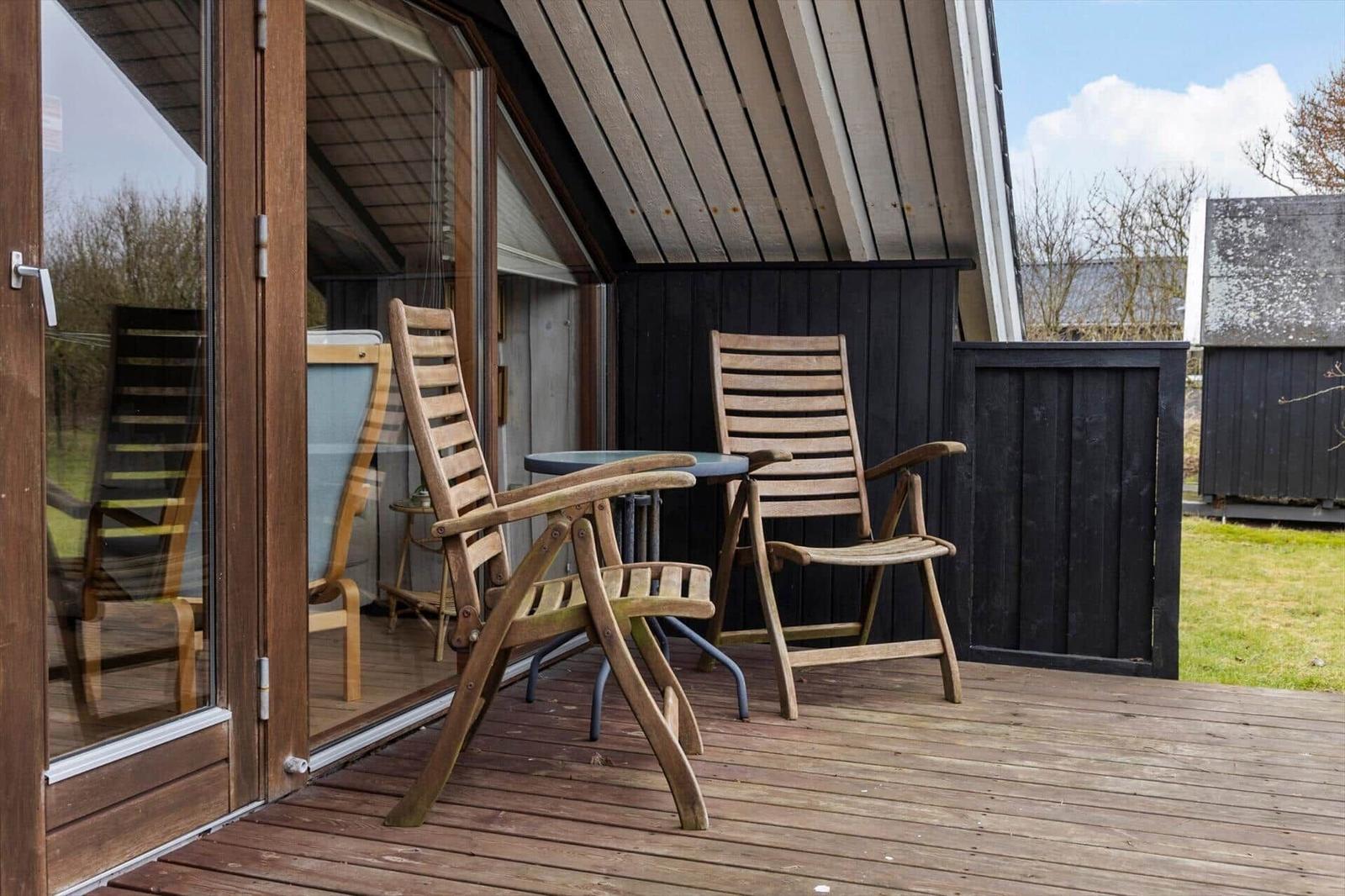 Terrasse mit zwei Holzstühlen und Tisch vor einem Haus mit Glasfront.