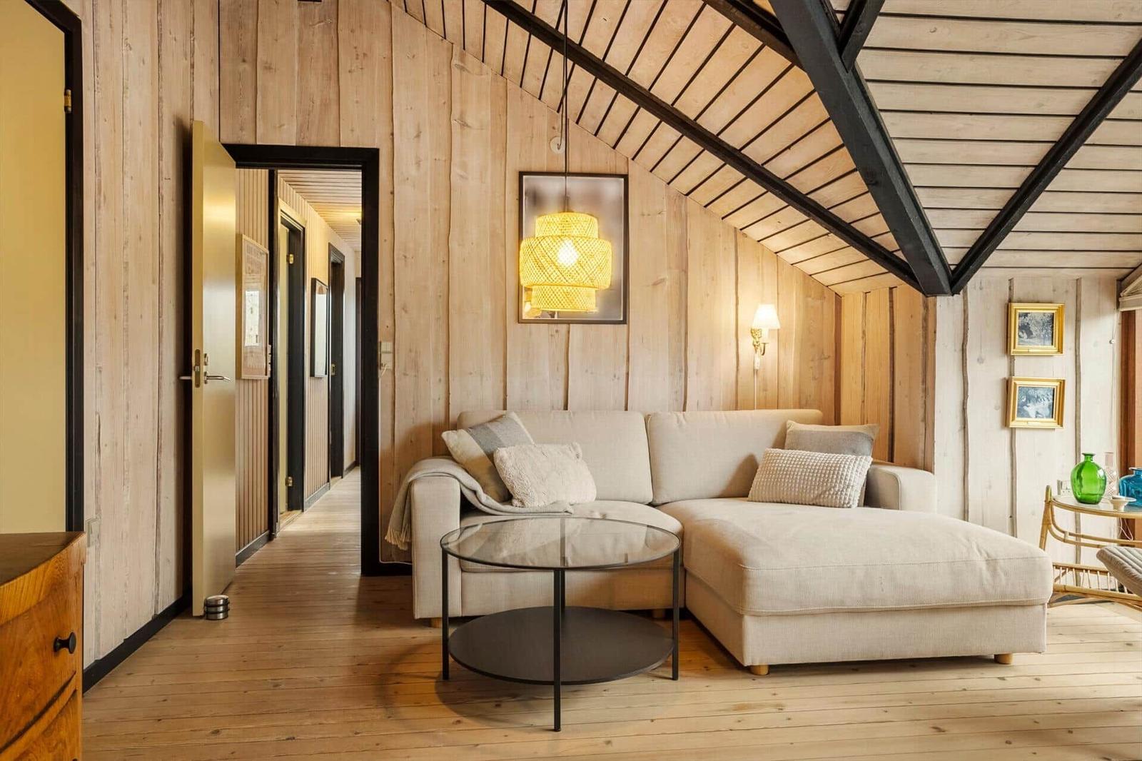 Wohnzimmer mit Sofa, Glas-Tisch und Holzwand. Decke mit Holzbalken.