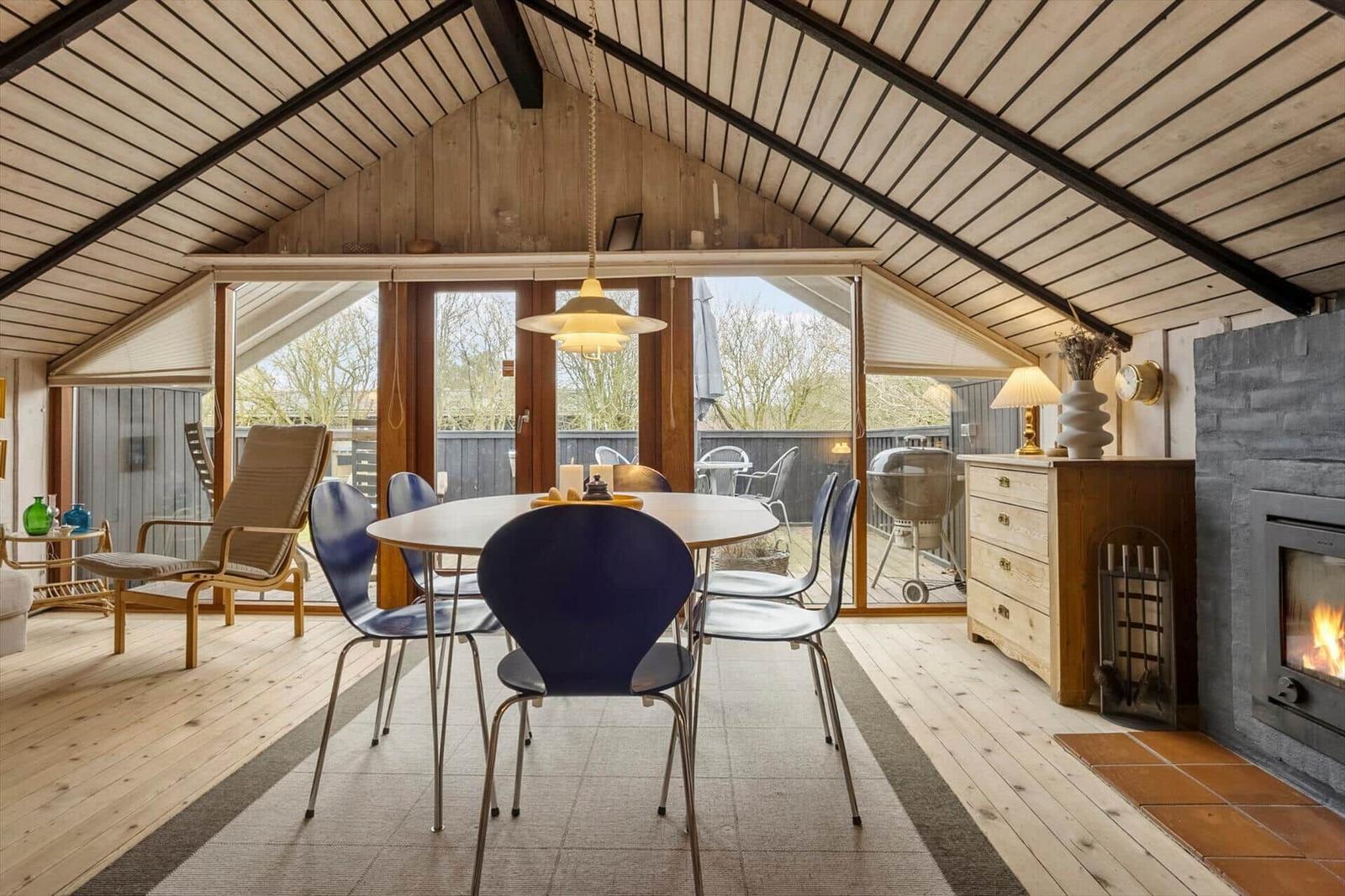 Essbereich mit Tisch, Stühlen und Kamin. Holzdecke und große Fenster.