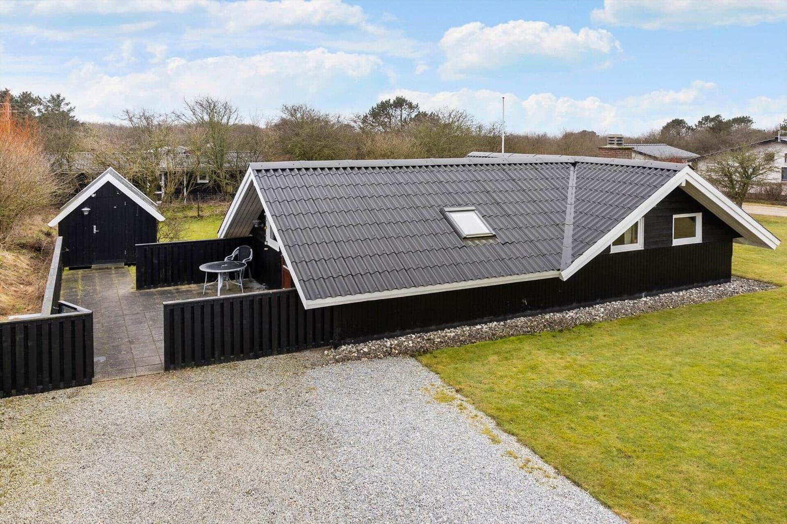 Schwarzes Haus mit Dachterrasse und Garten. Nebenhaus und Grillplatz sichtbar.