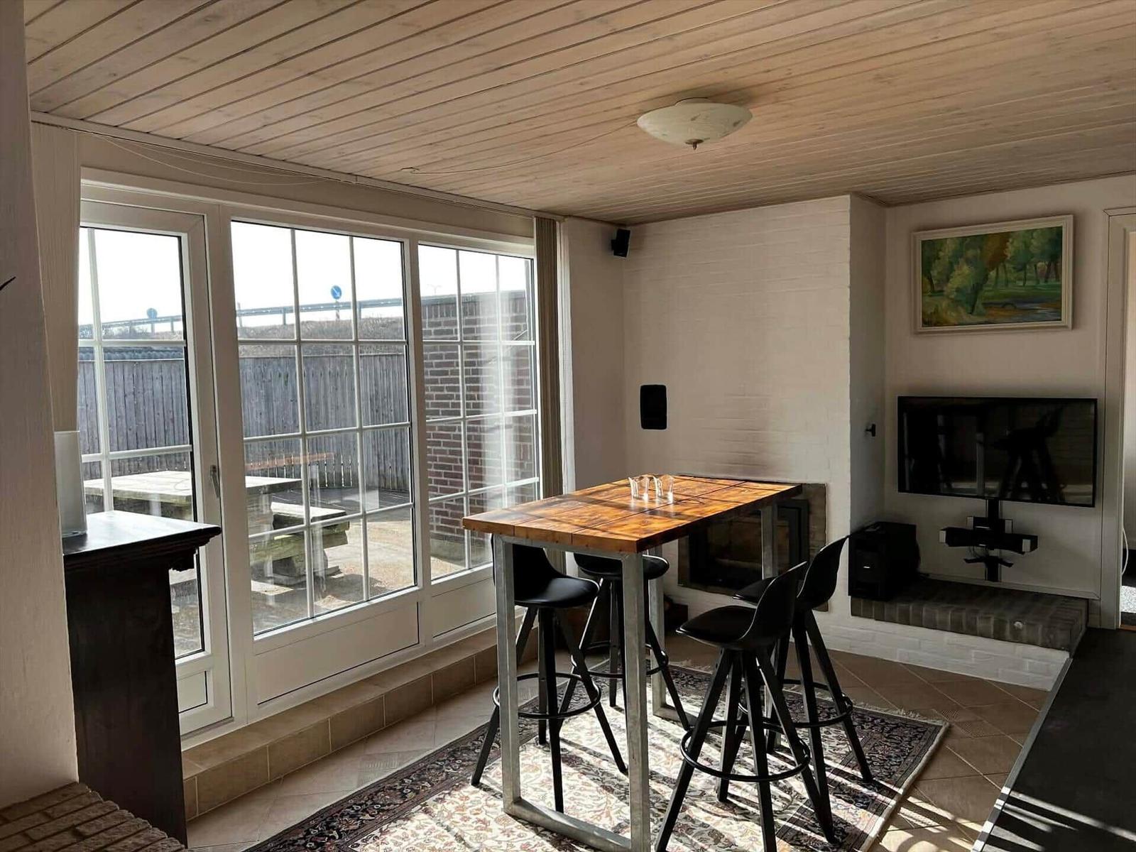 Raum mit Tisch, Stühlen, Fernseher und Fenster zur Außenterrasse.