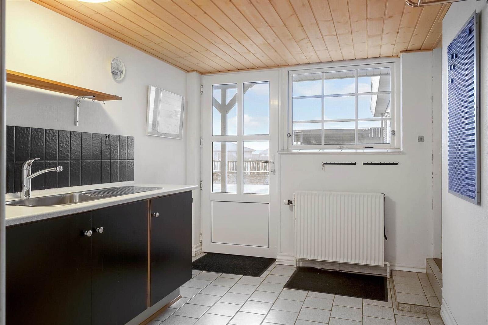 Küche mit dunklen Schränken, Arbeitsplatte und Fenster zur Außentür.