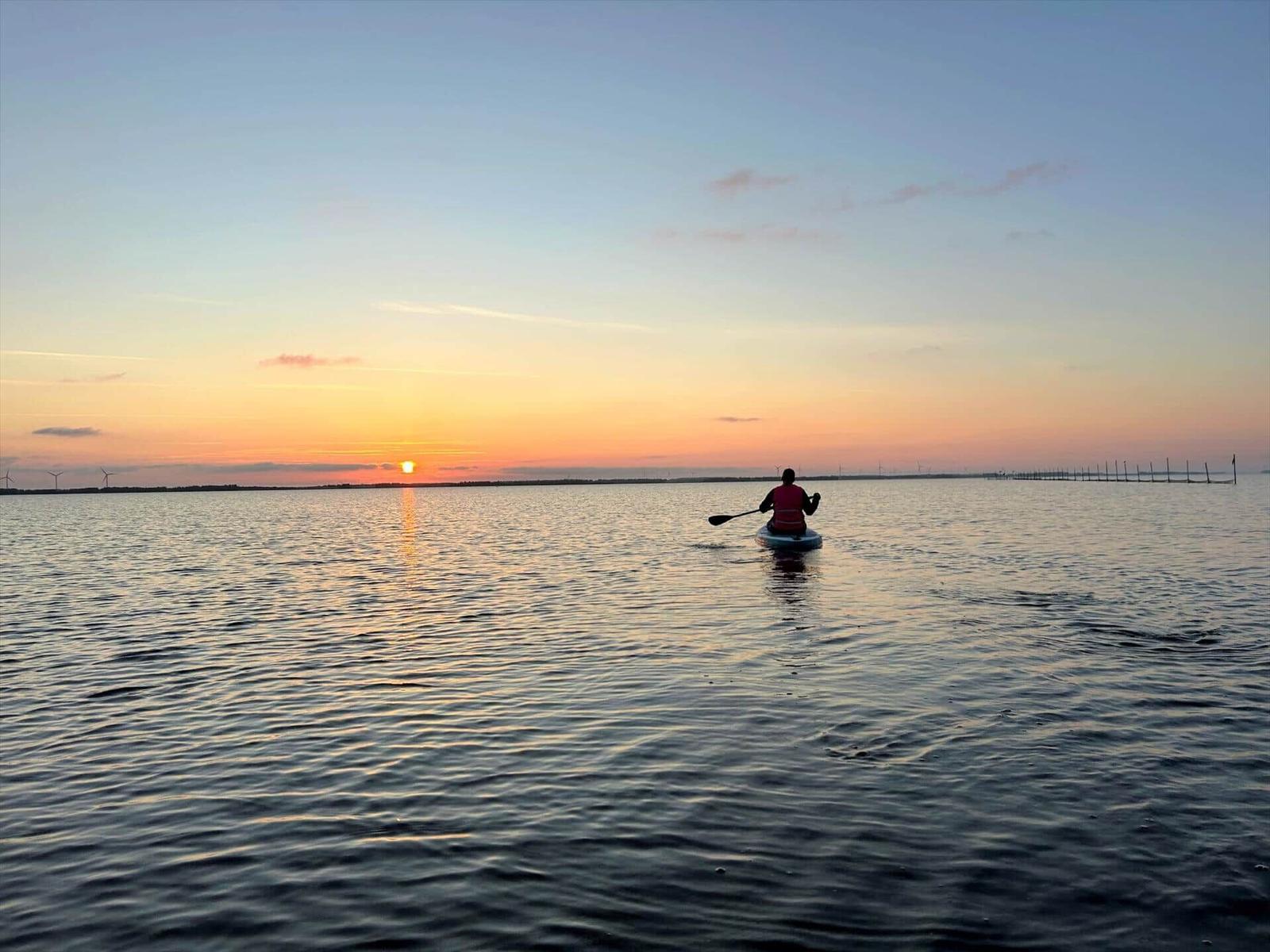 Ein Kajakfahrer paddelt auf ruhigem Wasser bei Sonnenuntergang.