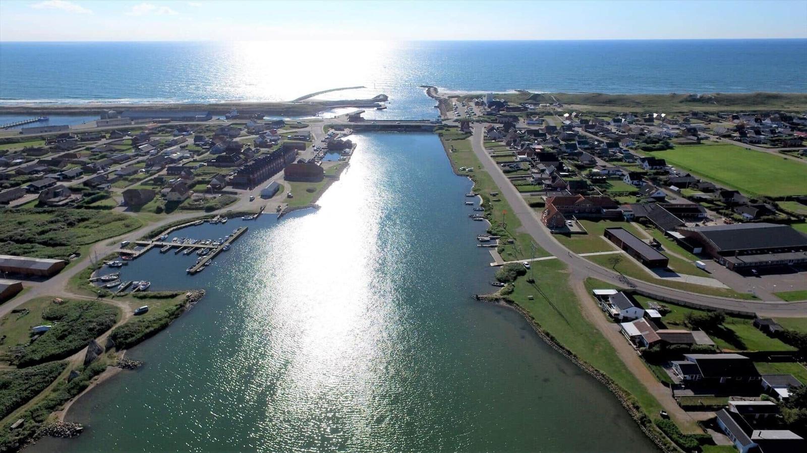 Aerial view of harbor with boats, coastal village, and open sea.
