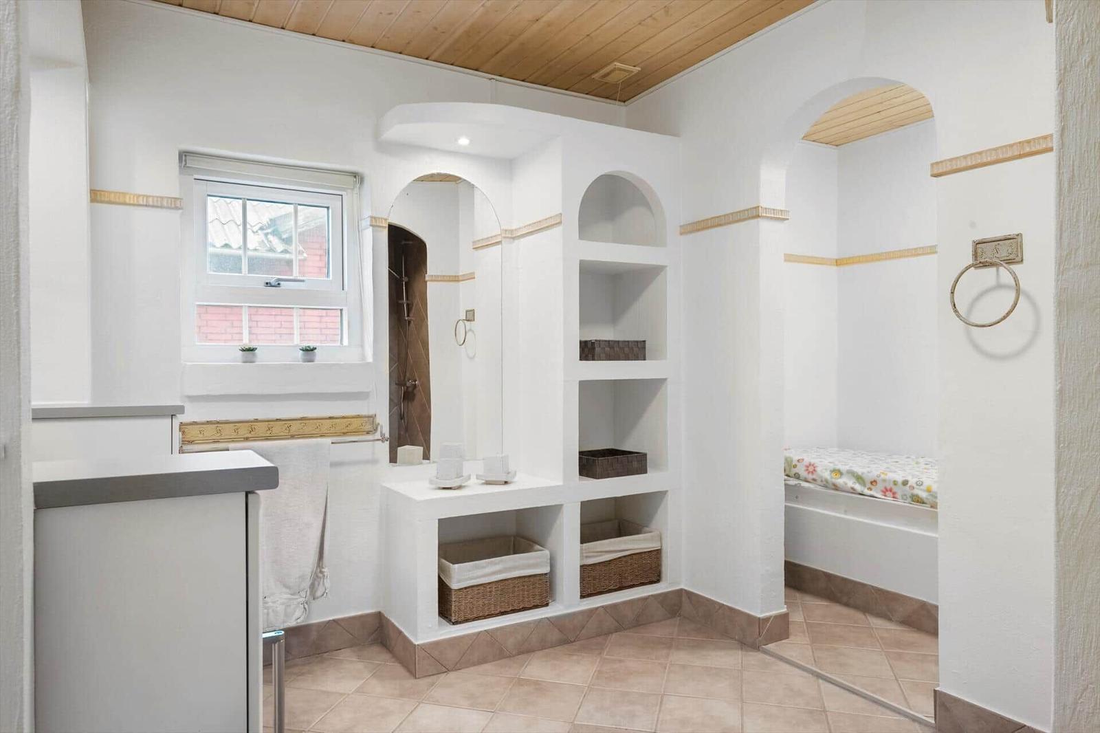 Badezimmer mit Dusche, Regalen und Fenster. Holzdecke und Fliesenboden.