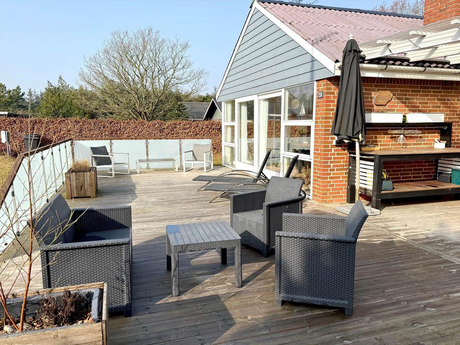 Terrasse mit Sitzgruppe, Sonnenliegen und Grillplatz an Hauswand.