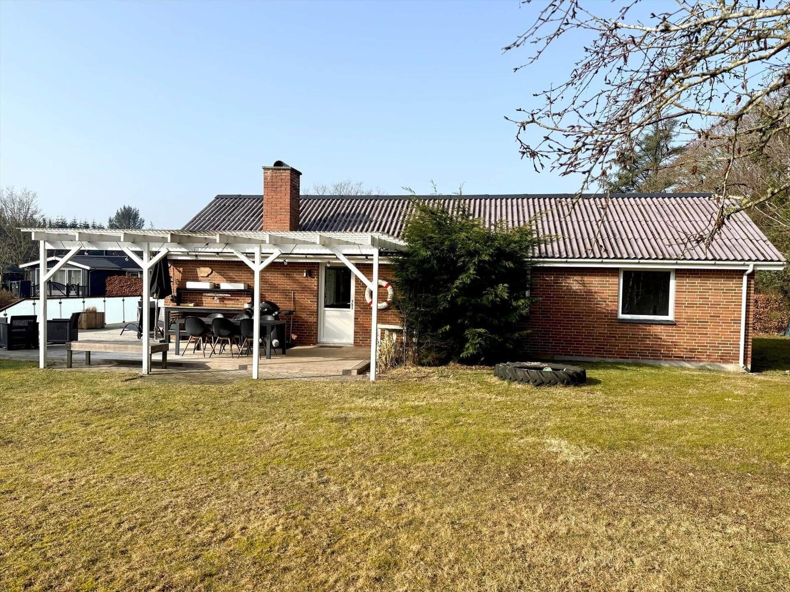 Ein Haus mit Terrasse, Grill und Garten. Ein Schornstein ragt aus dem Dach.