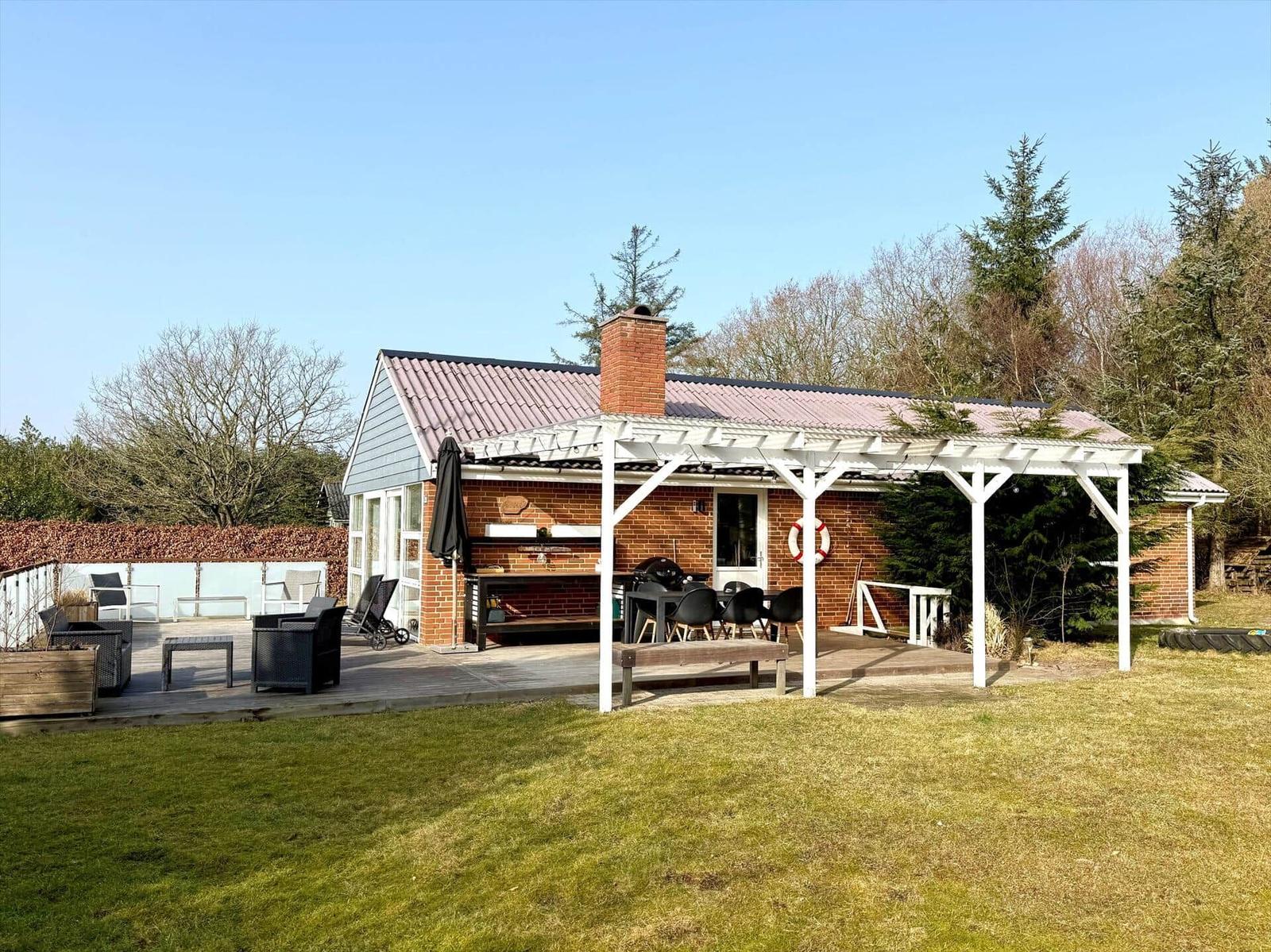 Haus mit Terrasse, Grillbereich und Garten. Weiße Veranda mit Tisch und Stühlen.