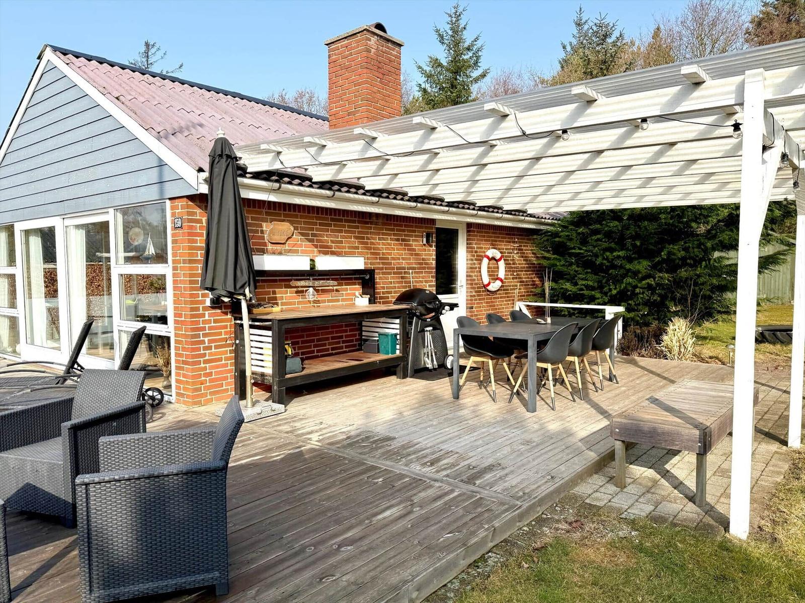 Terrasse mit Grill, Tisch, Stühlen und Sonnenschutz. Holzdecke und Gartenbereich.