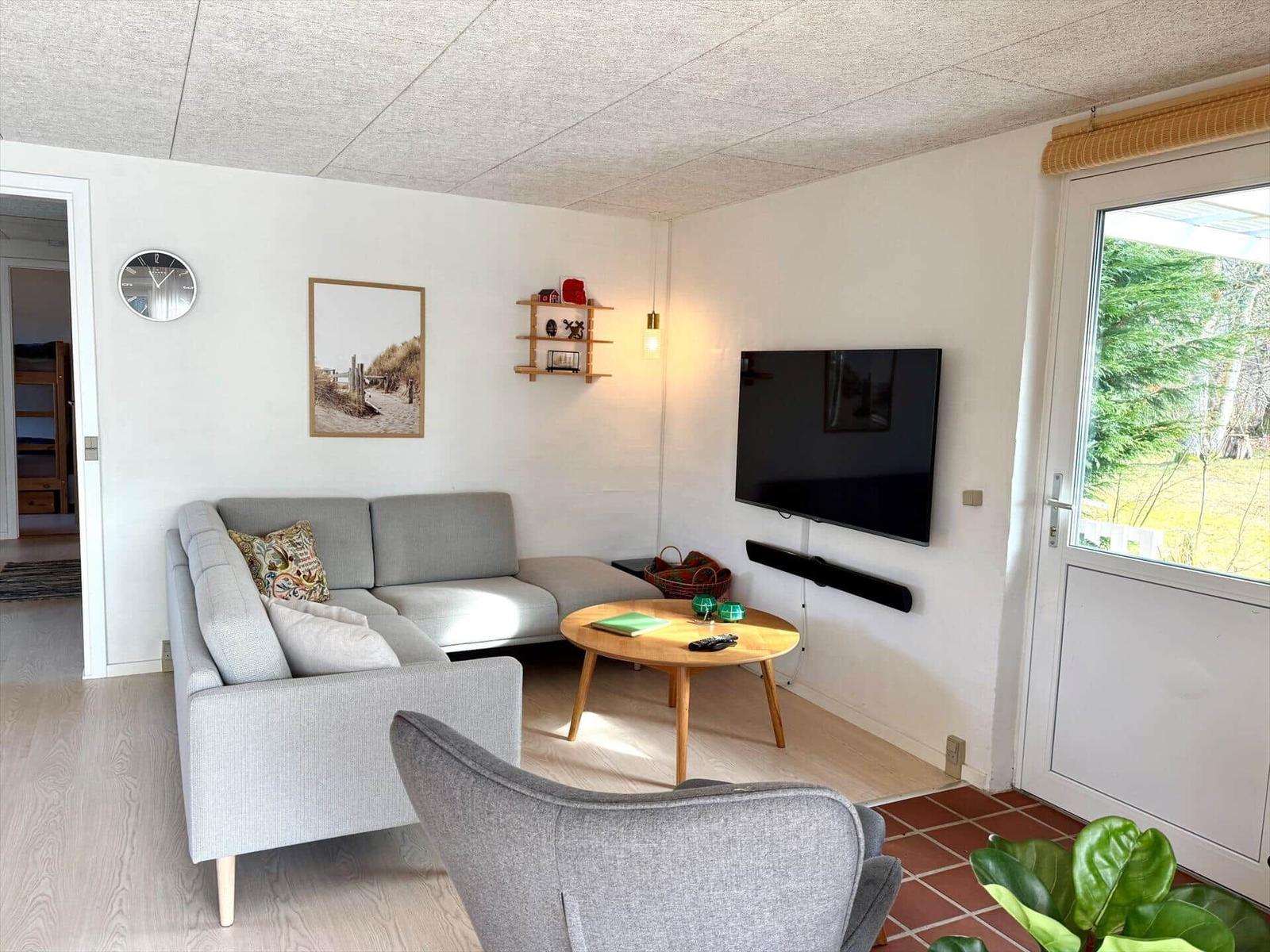 Wohnzimmer mit Sofa, Fernseher und Tisch. Durchgang zur Schlafzimmer.