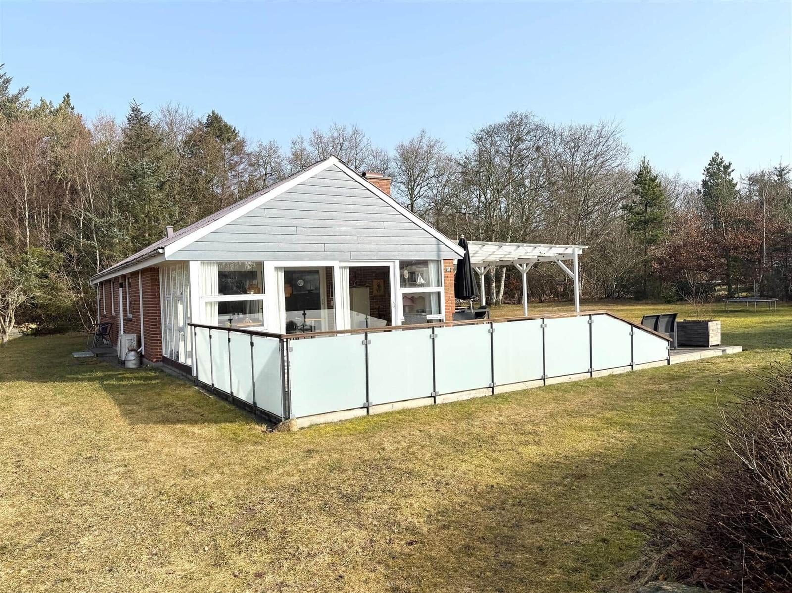 Haus mit Terrasse und Garten. Holzveranda und Glasgeländer sichtbar.