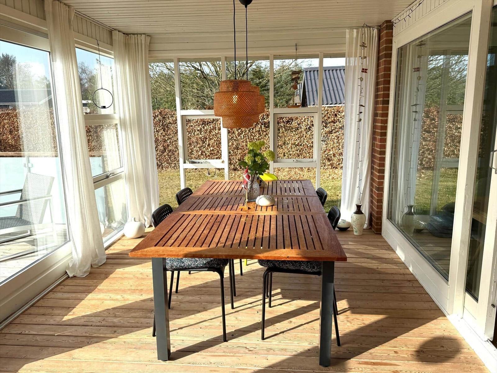 Terrasse mit Holztisch und Stühlen, großzügige Glaswände und Deckenleuchte.