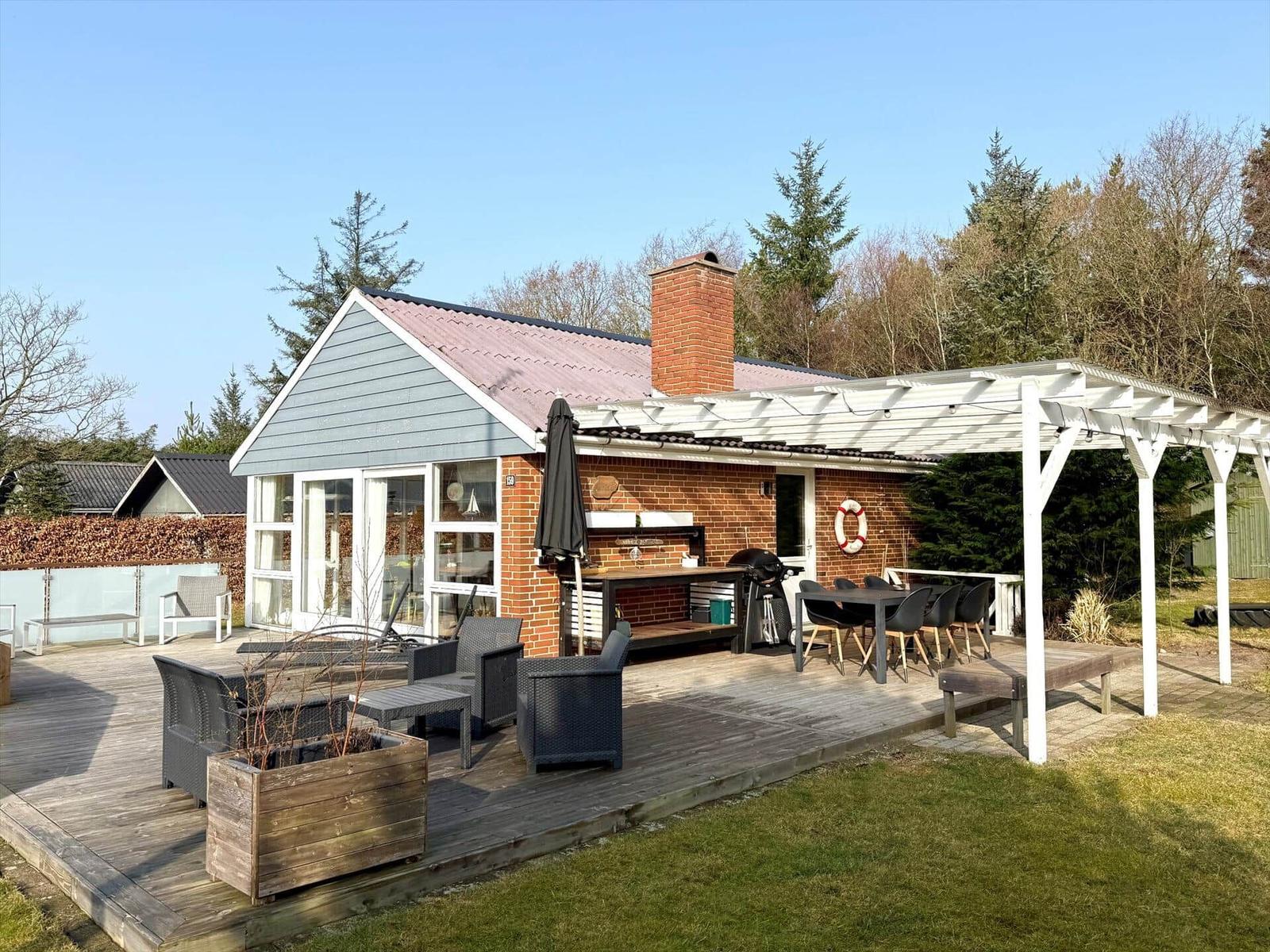 Haus mit Terrasse, Grill und Sitzgelegenheiten im Freien.