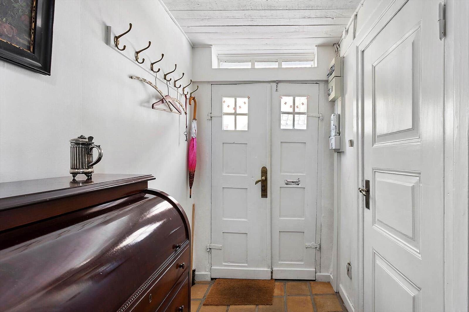 Entrance with white door, coat hooks, and wooden cabinet.