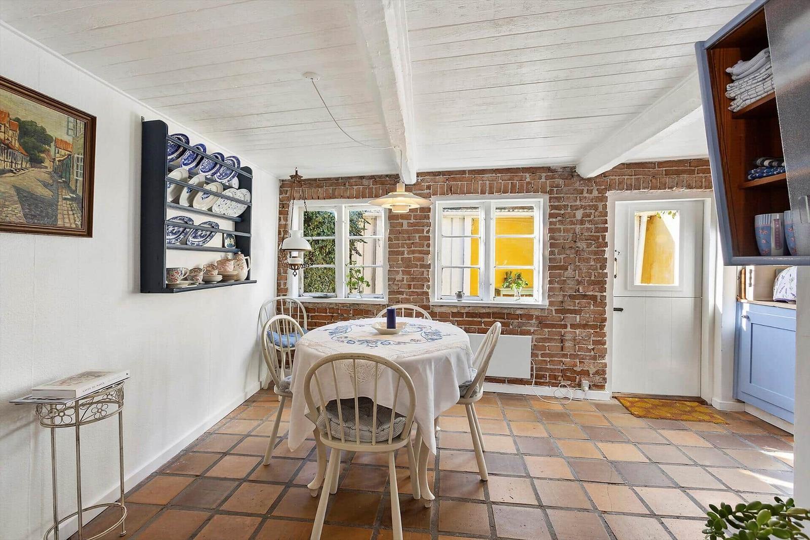 Dining room with table, chairs, brick wall, and terracotta floor.