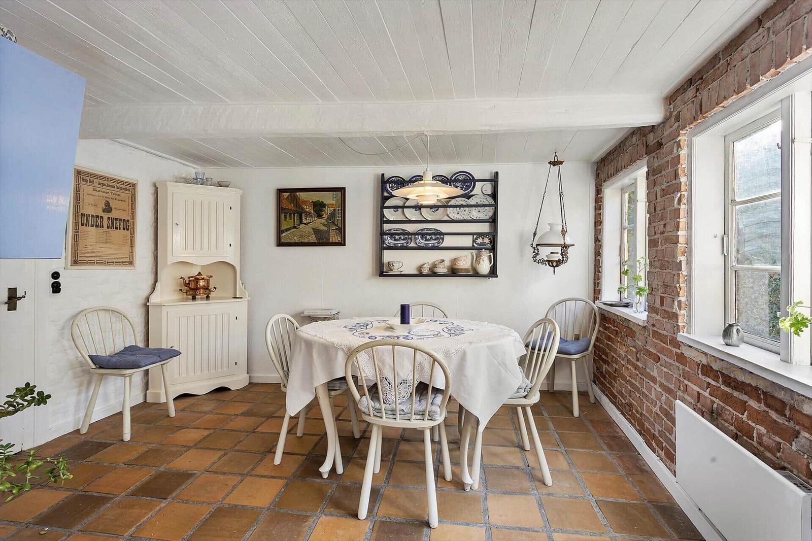 Dining room with round table, white chairs, and brick wall