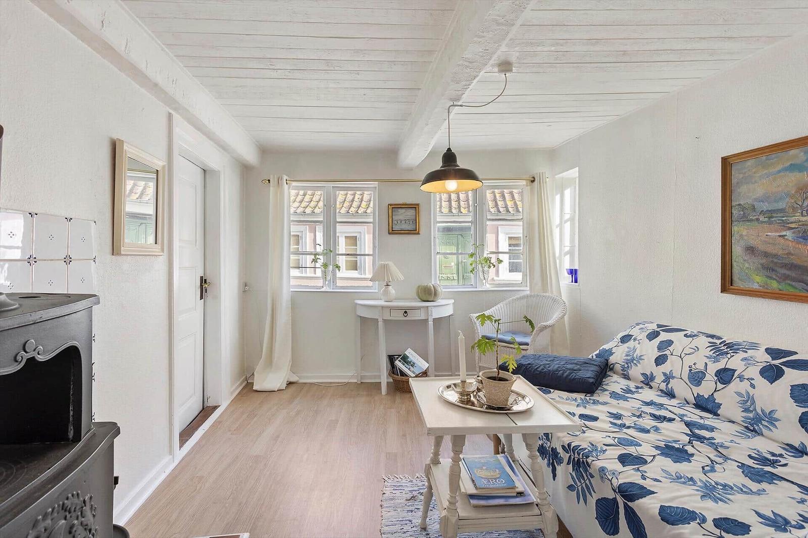 A living room with blue and white sofa, wooden floor and white walls. A picture hangs on the wall.
