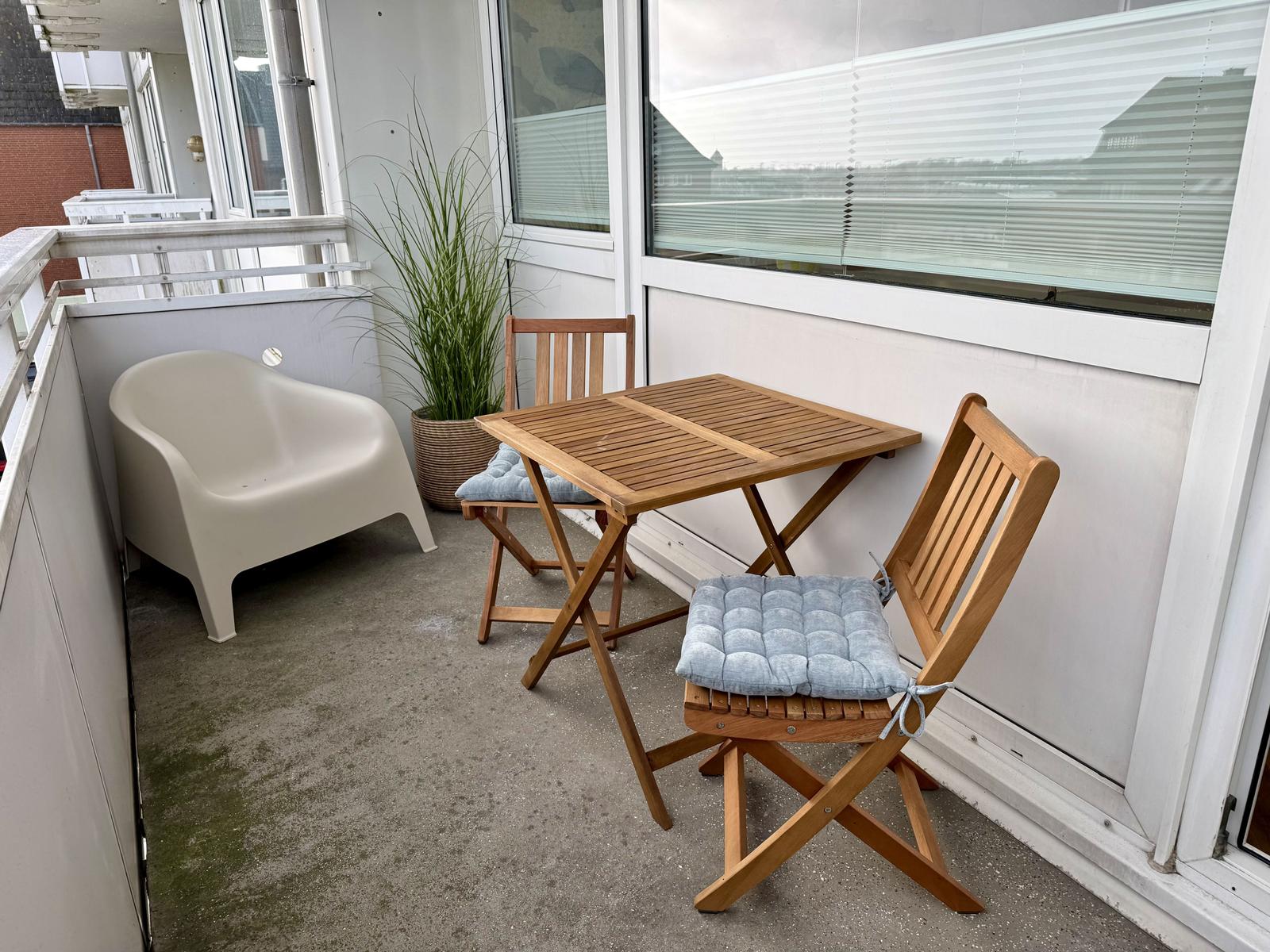 Terrasse mit Tisch, zwei Stühlen und Pflanze. Weiße Sitzgelegenheit daneben.