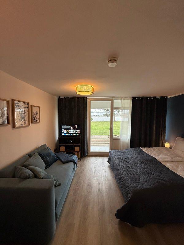 Bedroom with bed, sofa, and TV. Doorway to terrace with view of green area.