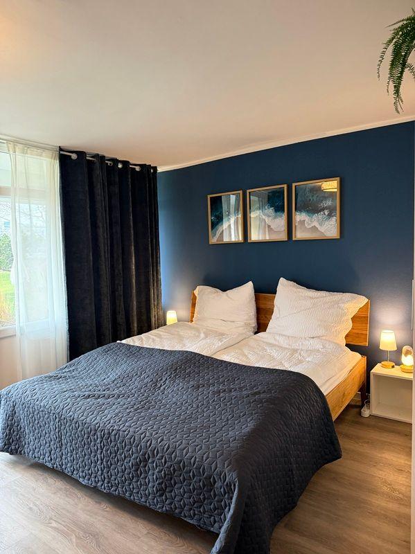 Bedroom with bed, blue wall, and window with curtains.