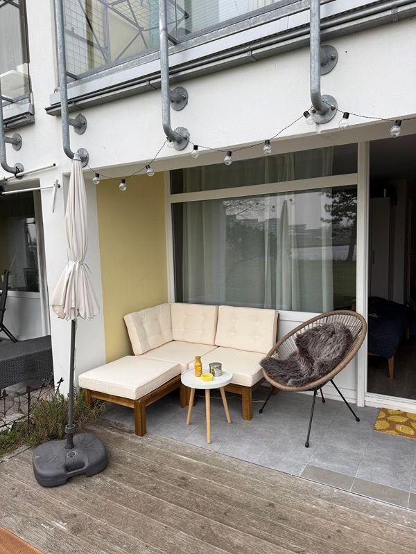 Terrace with seating group, round chair, and table under utility pipes.