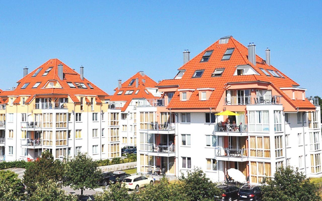 Mehrfamilienhaus mit rotem Dach und Balkonen unter blauem Himmel.