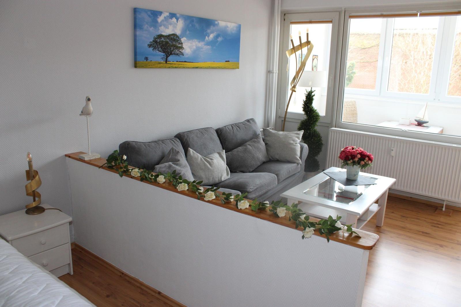 Wohnbereich mit grauem Sofa, weißen Möbeln und Fensterblick.
