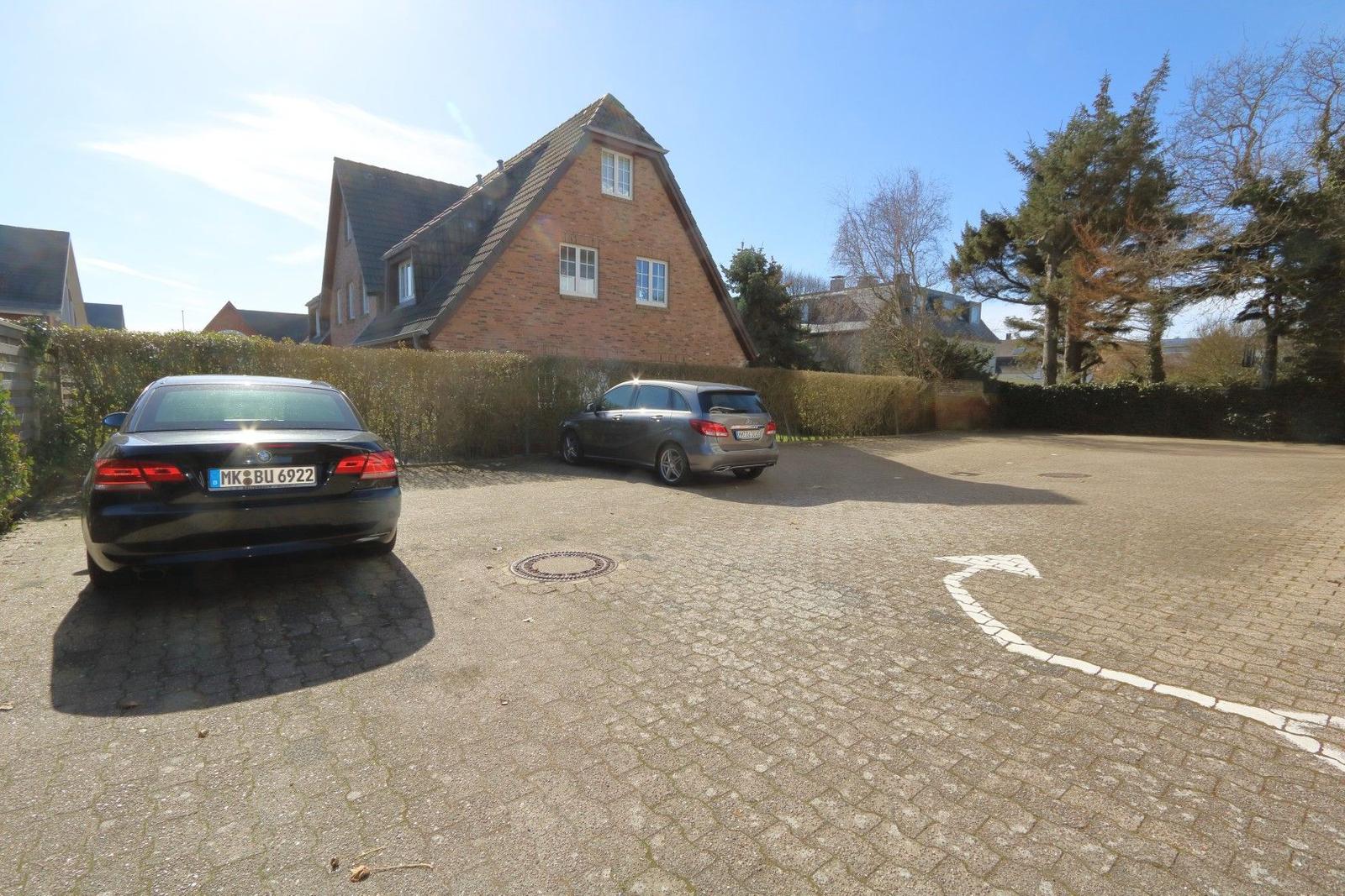 Zwei Autos parken auf einem gepflasterten Hof vor einem Haus mit Ziegelfassade.