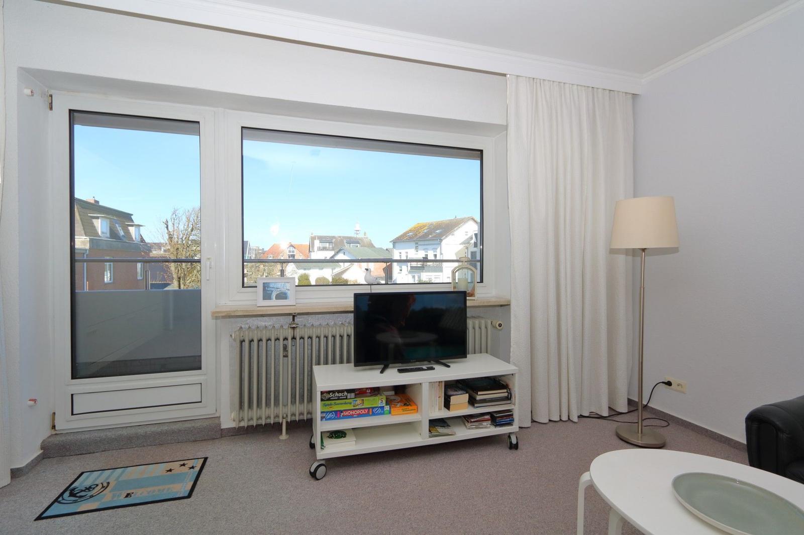 Wohnzimmer mit TV, Bücherregal und Balkonansicht