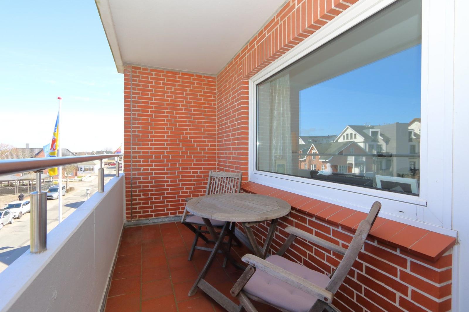 Balkon mit Tisch und Stühlen, rote Ziegelwand, Fenster mit Blick auf Gebäude.