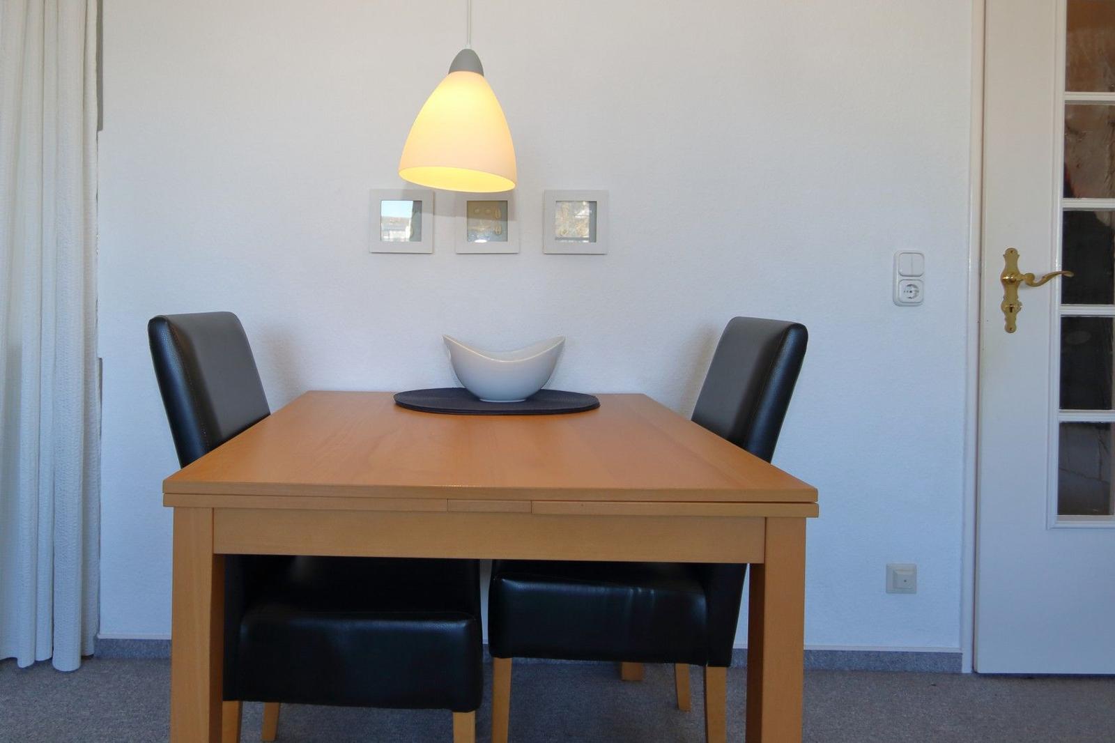 Esszimmer mit Holztisch, zwei schwarzen Stühlen und einer Deckenlampe.