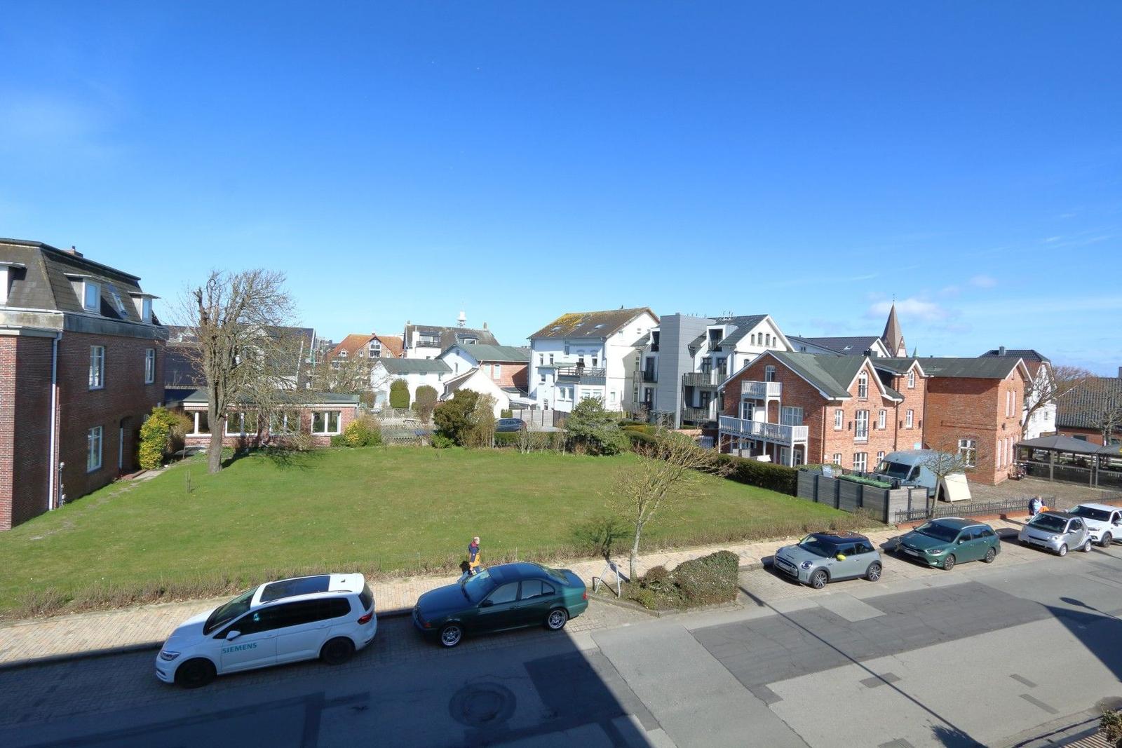 Grüner Rasenbereich mit geparkten Autos und Wohnhäusern im Hintergrund.