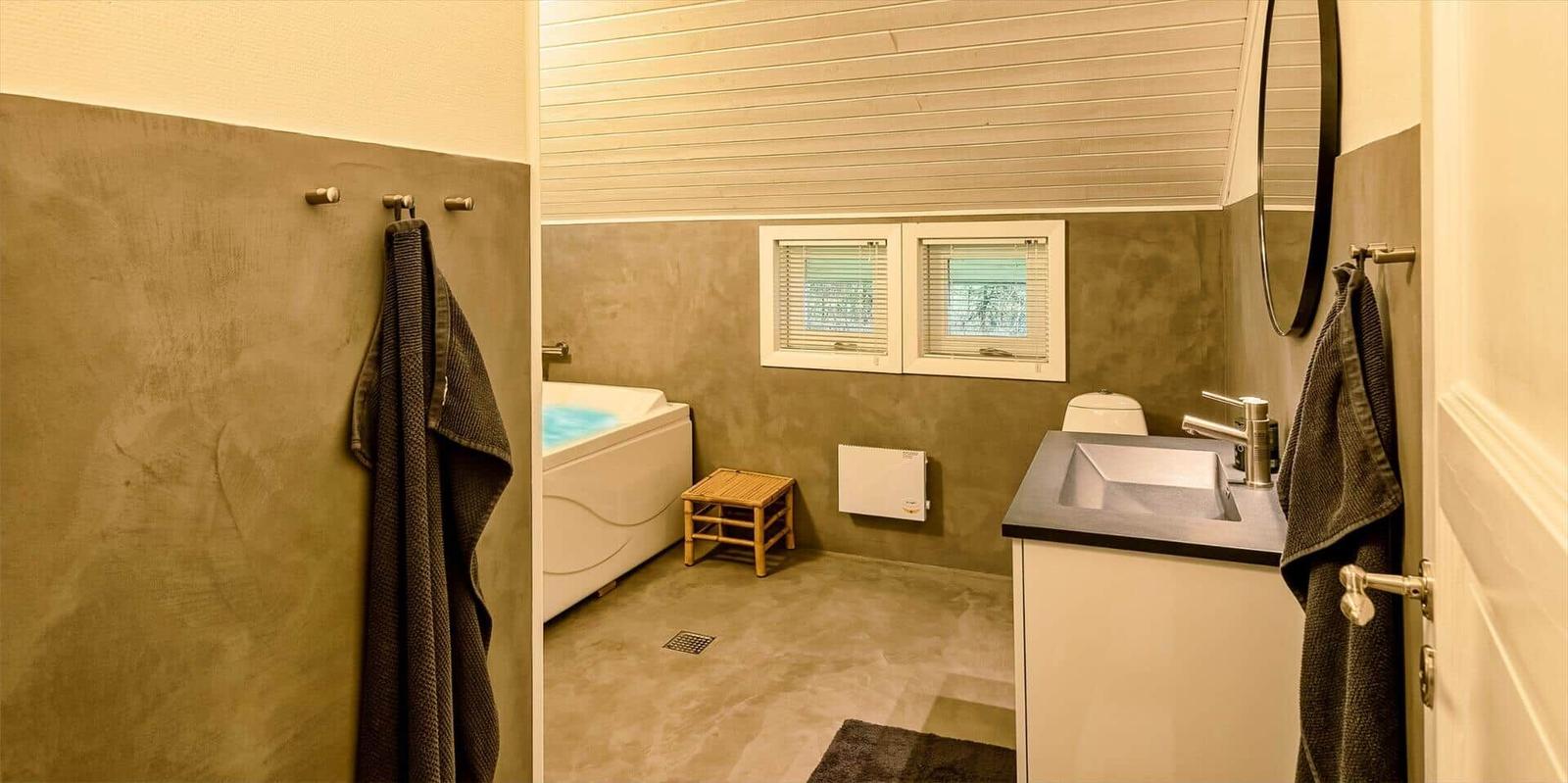 Badezimmer mit Badewanne, Waschbecken und Toilette. Zwei Fenster und Holzdecke.