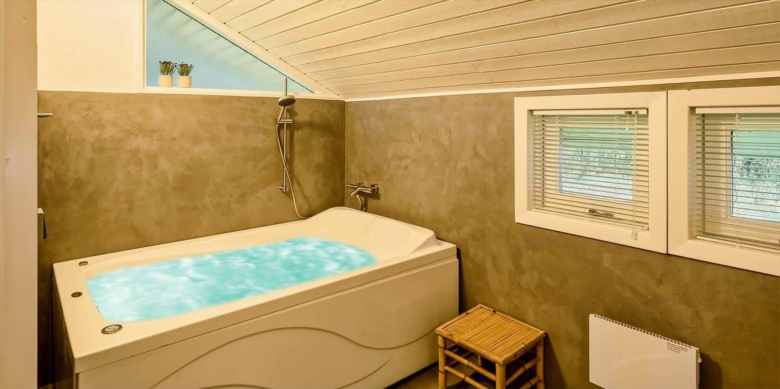 Bad mit Whirlpool, Dusche und zwei Fenstern mit Jalousien.