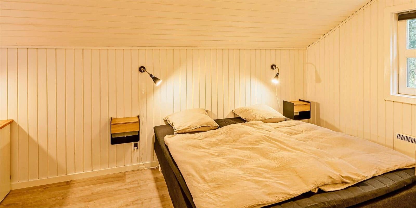Schlafzimmer mit Doppelbett, zwei Nachttischen und Wandlampen an vertikal verkleideten Wänden.