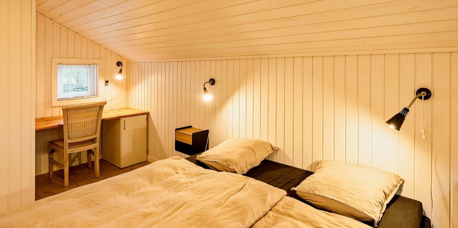 Schlafzimmer mit Bett, Nachttisch, Schreibtisch und Fenster.
