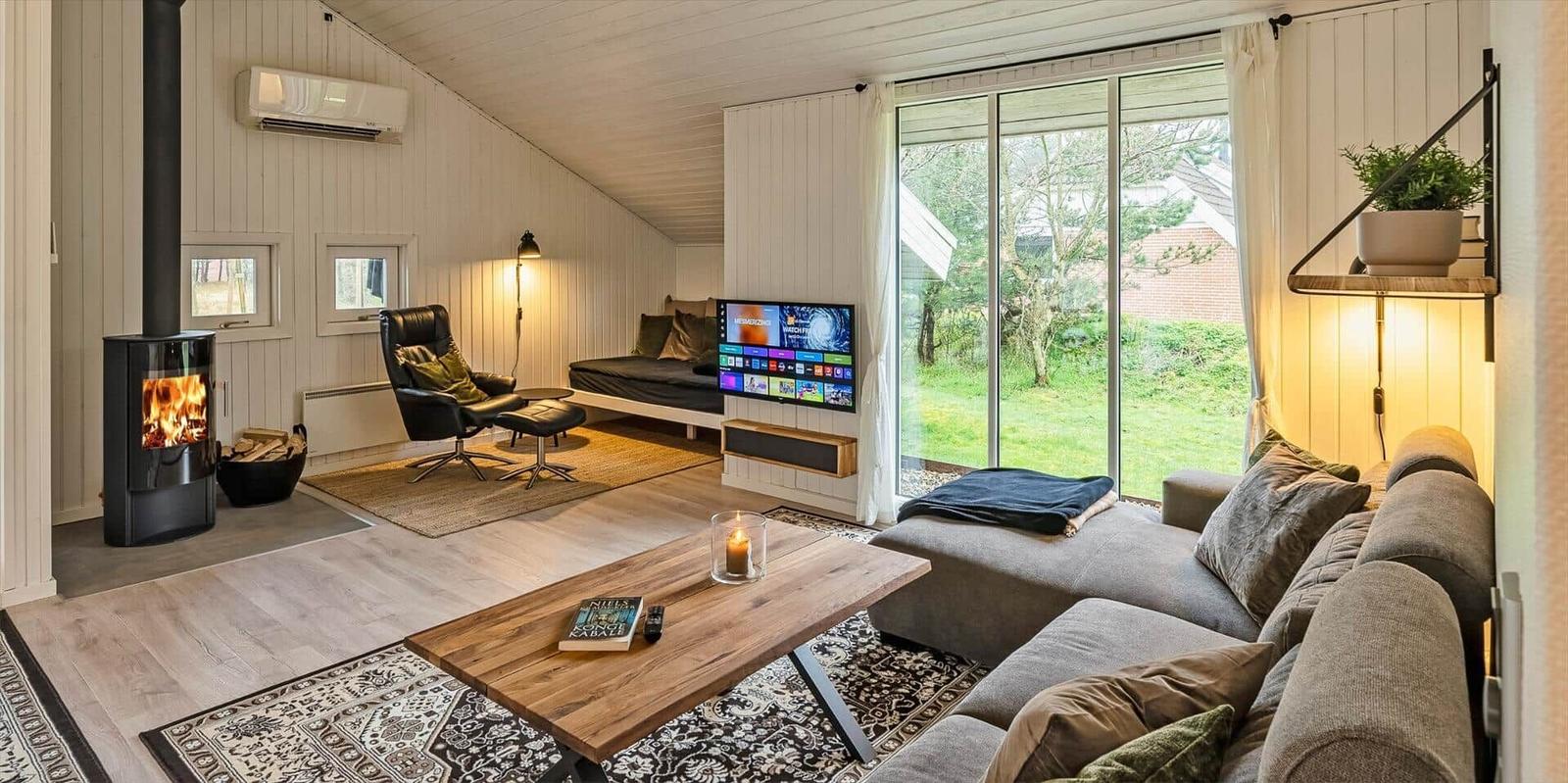 Wohnzimmer mit Kamin, TV und großem Fenster. Holzboden und Sofa.