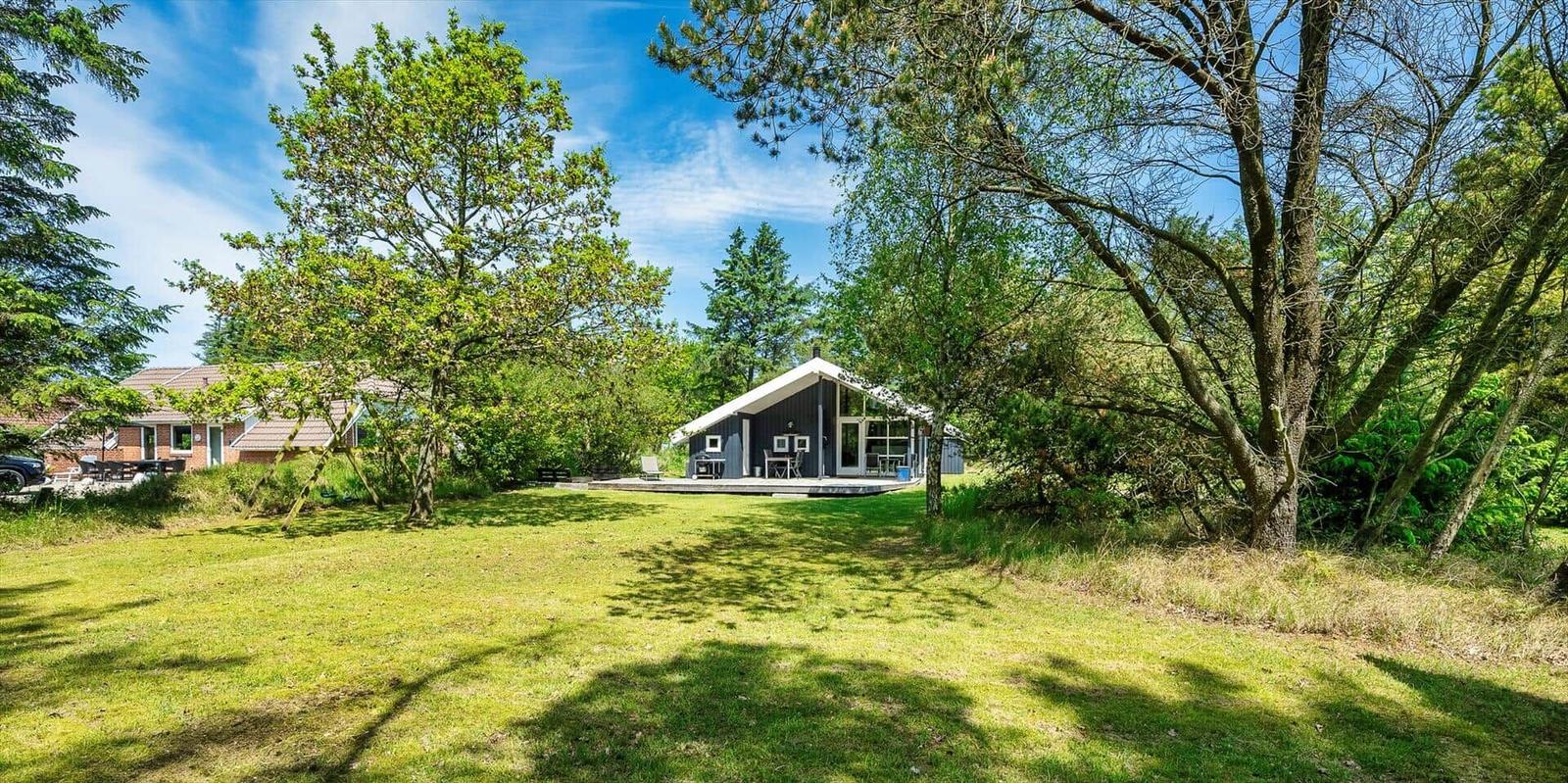 Moderne Hütte mit Terrasse in grüner Umgebung unter blauem Himmel.