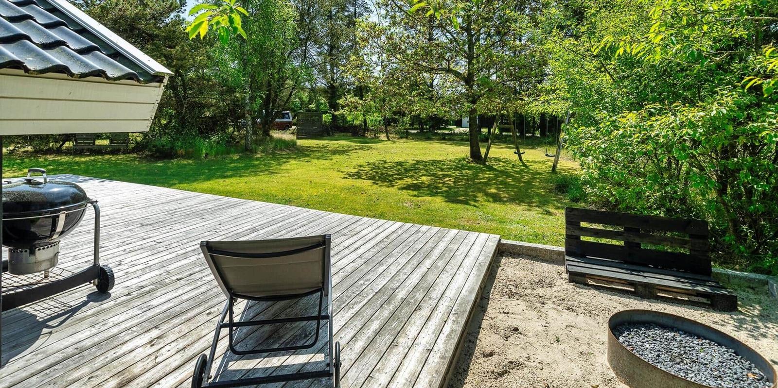 Terrasse mit Grill, Liegestuhl und Sandkasten. Grasfläche und Bäume im Hintergrund.