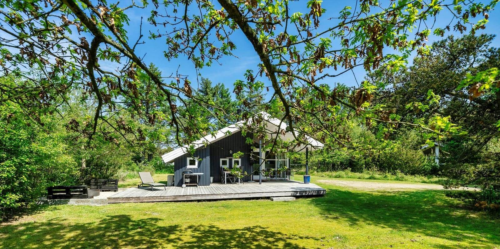 Ein kleines Haus mit Terrasse steht inmitten von Bäumen und Gras.