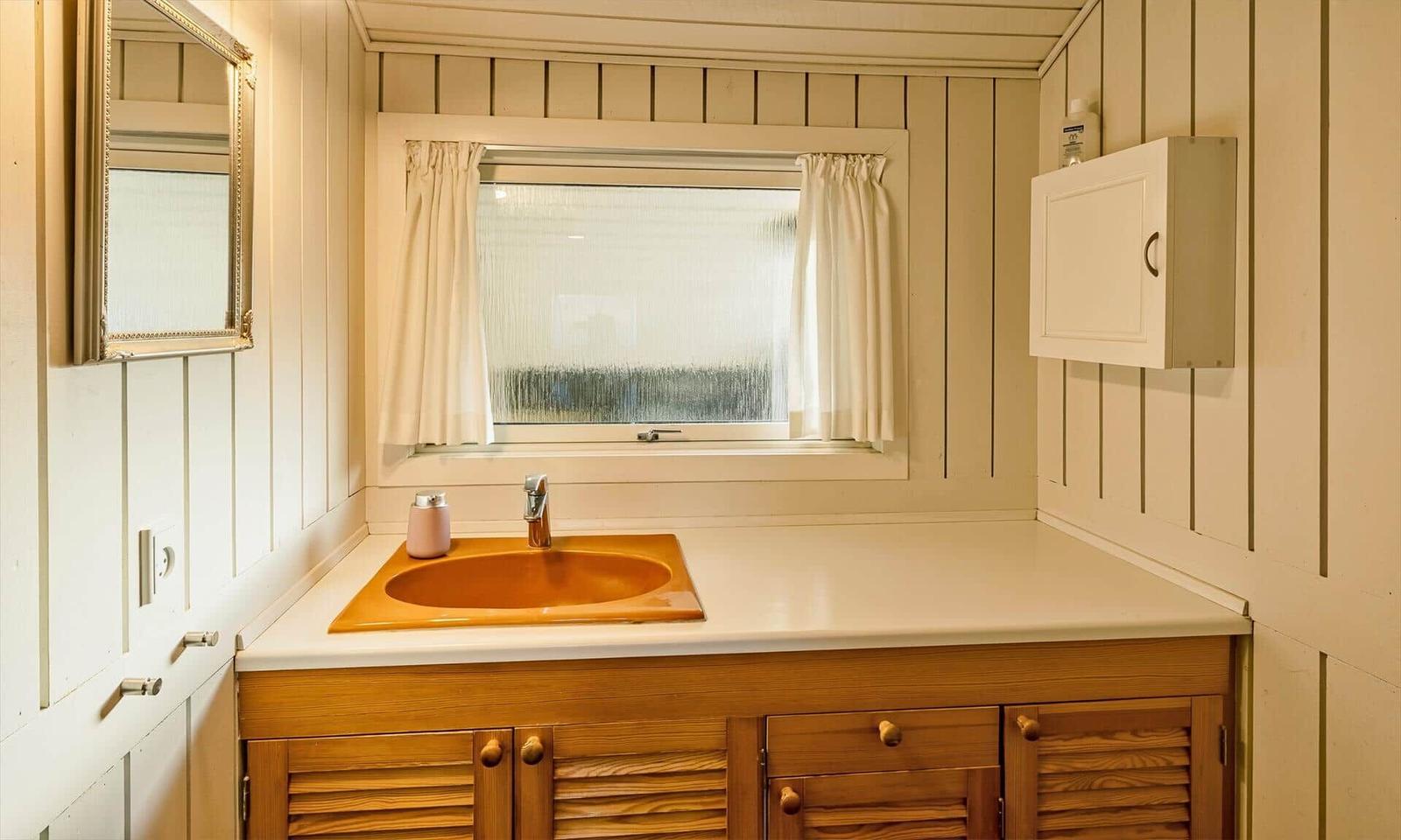 Badezimmer mit Waschbecken, Spiegel und Fenster mit Vorhängen.